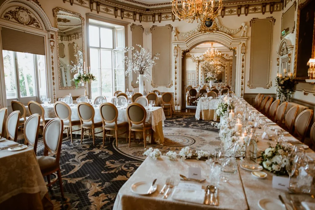 Elegant wedding reception set in an ornate ballroom with chandeliers, candlelit tables and white floral arrangements