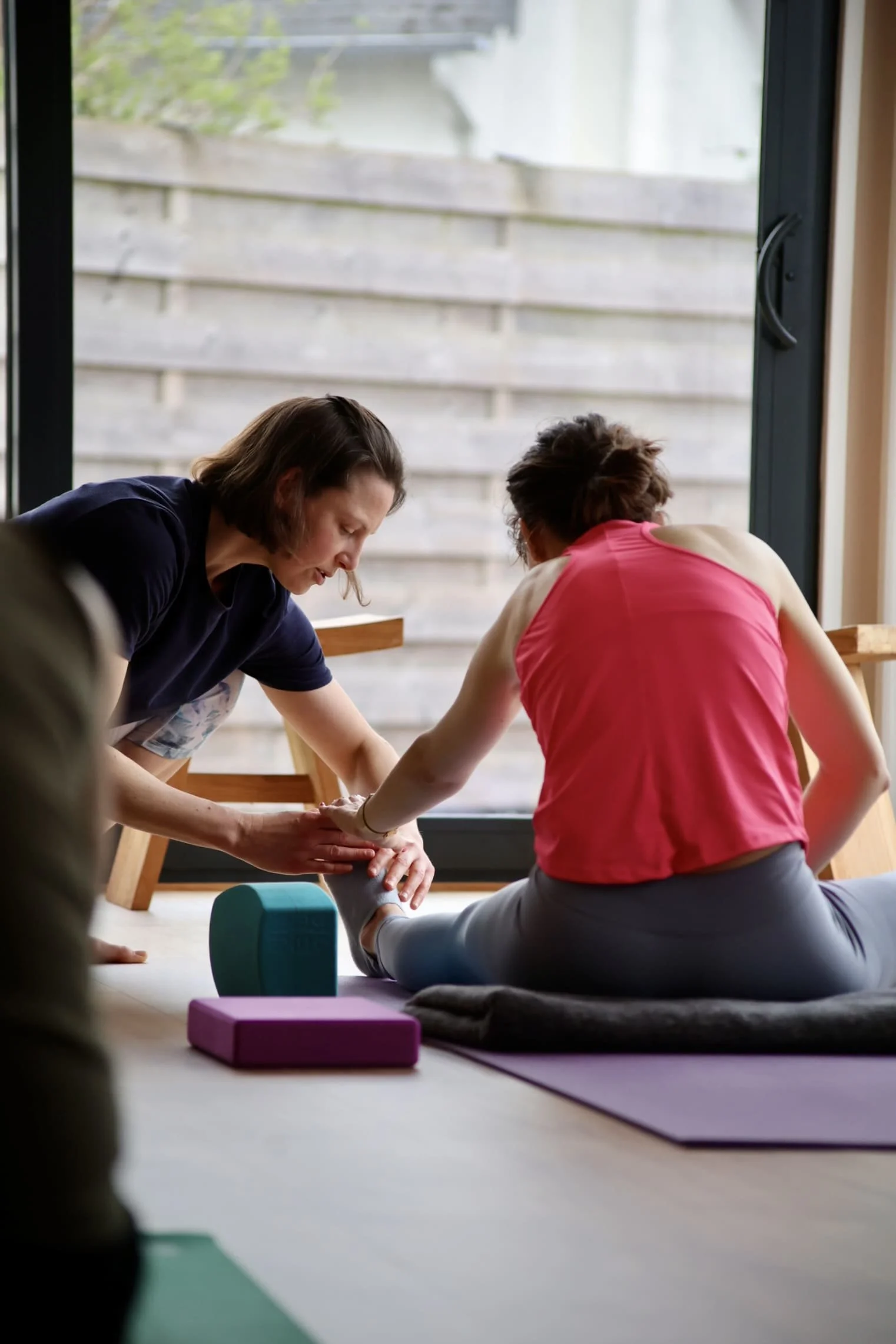 Eugénie, la professeure yoga, aide une élève à trouver sa posture de yoga, une posture d'étirement assise au sol.