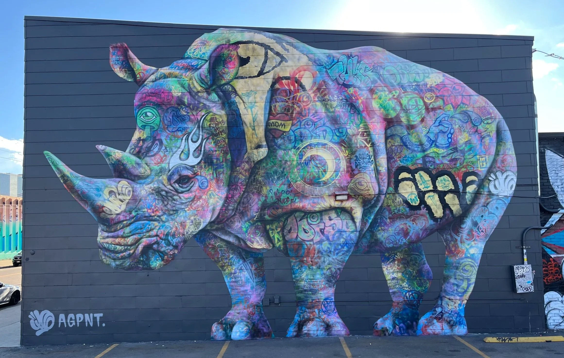 Colorful mural of a rhinoceros painted on a large exterior wall, featuring graffiti-style designs and various symbols, with a dark background.