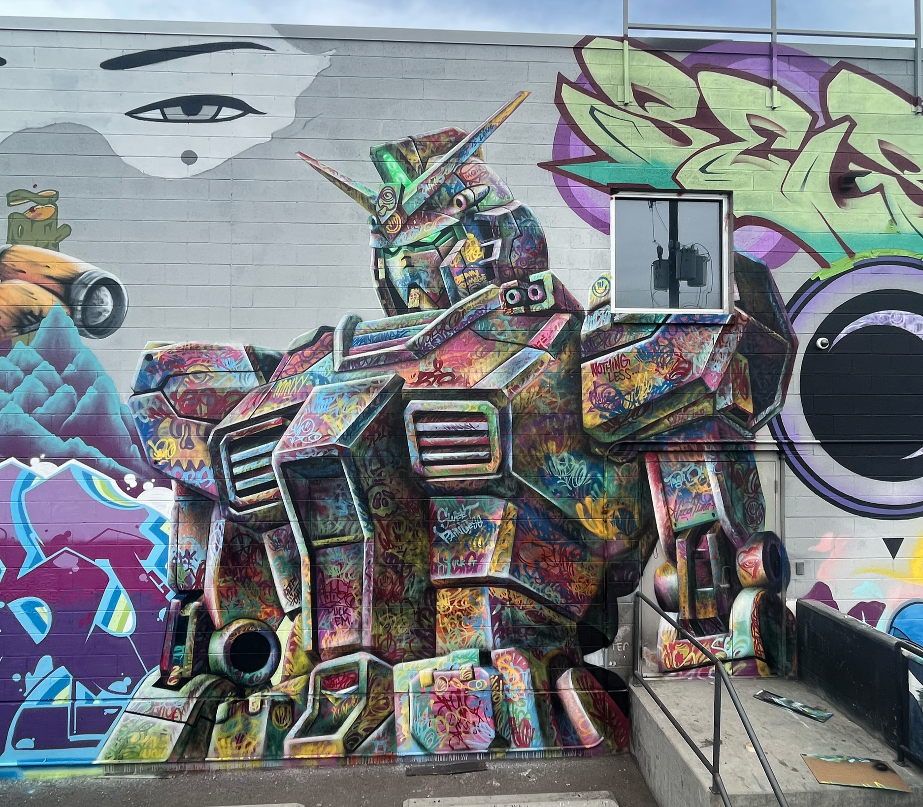 Colorful graffiti mural of a giant robot with a humanoid face and a unicorn horn, painted on an exterior brick wall, with various graffiti designs surrounding it.
