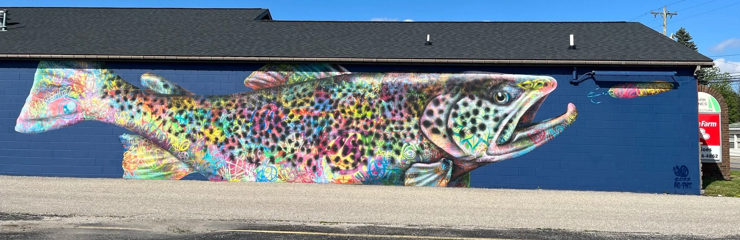 Colorful mural of a fish painted on a blue building wall.