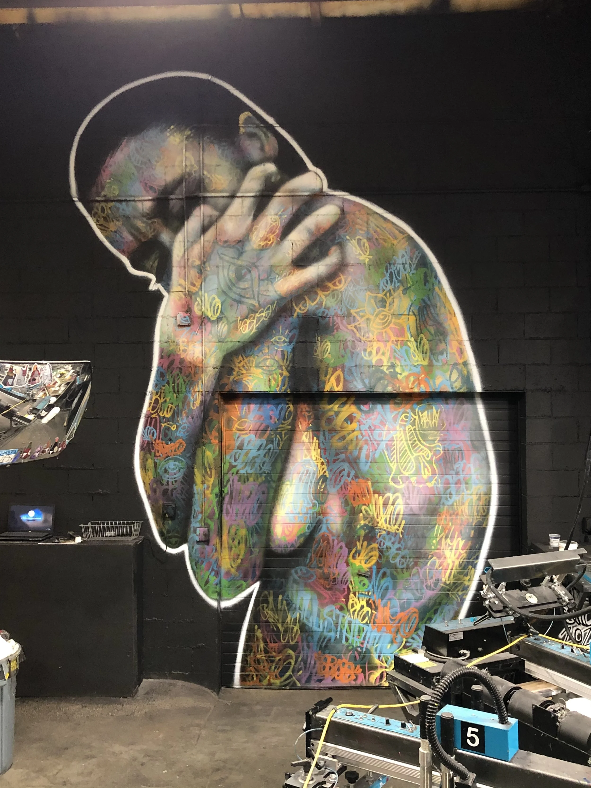 Colorful graffiti artwork of a person with head bowed and hand on neck, painted on a wall.