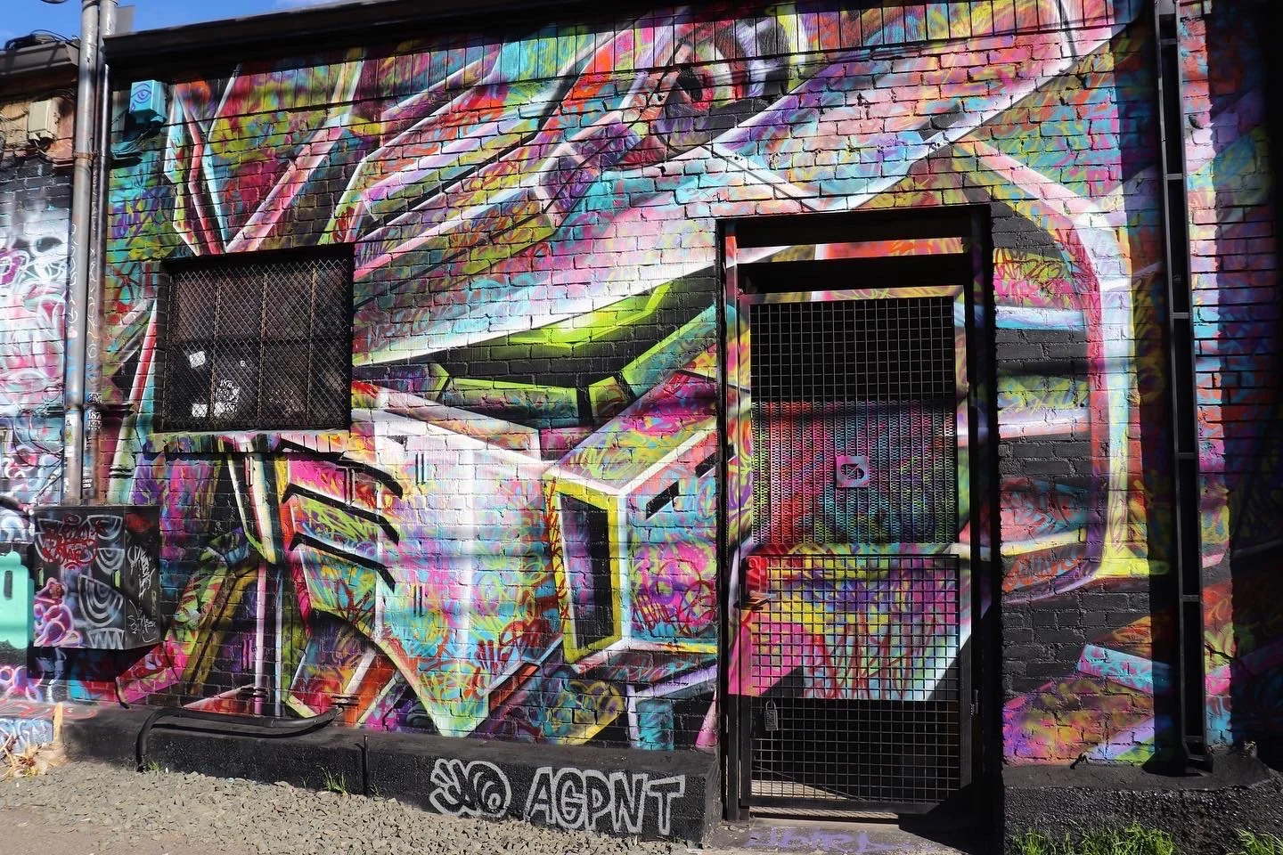 Colorful graffiti art of a robot's face on a brick wall with a metal gate and vent.