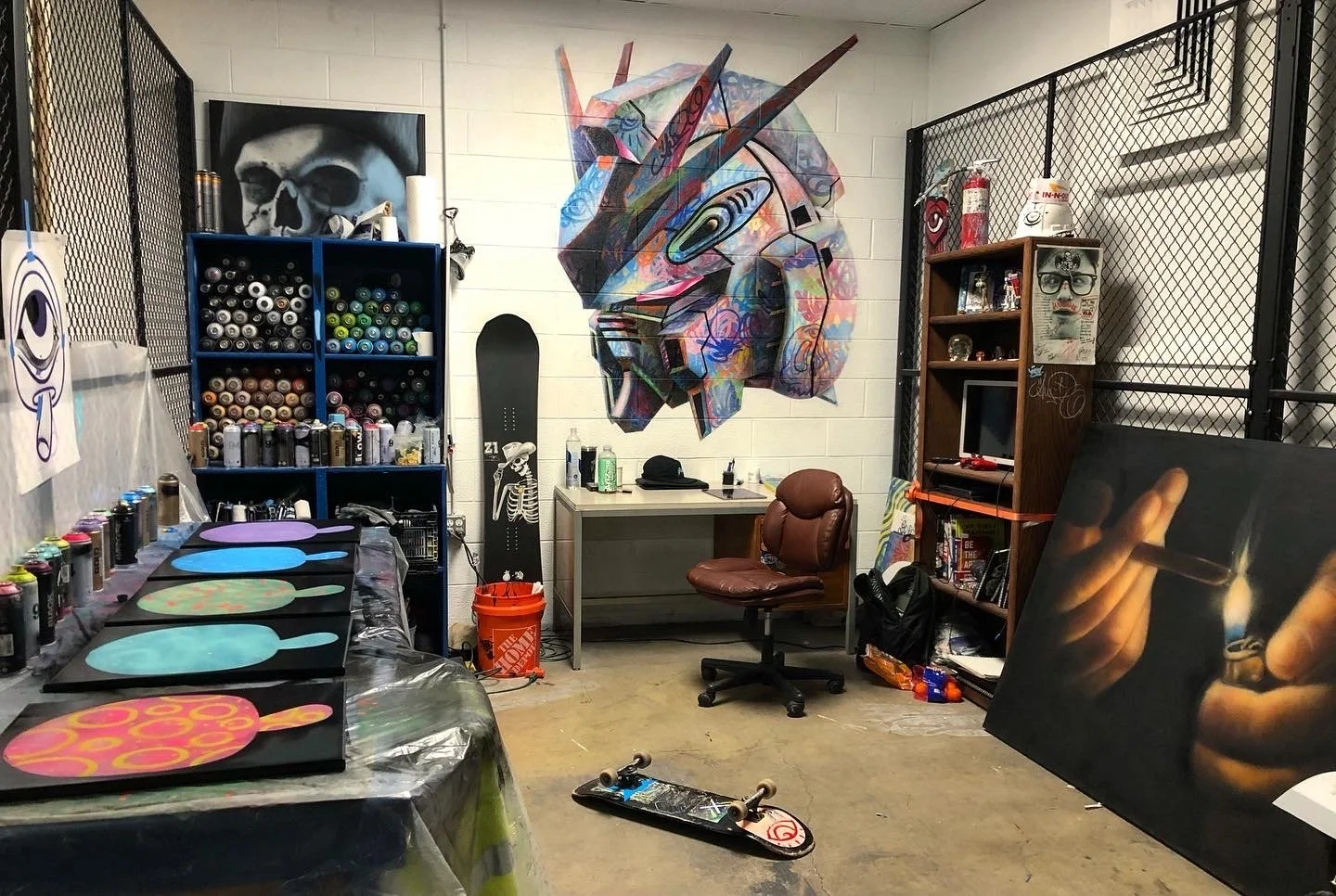 Art studio with spray paint cans, skateboard, and colorful mural on the wall.