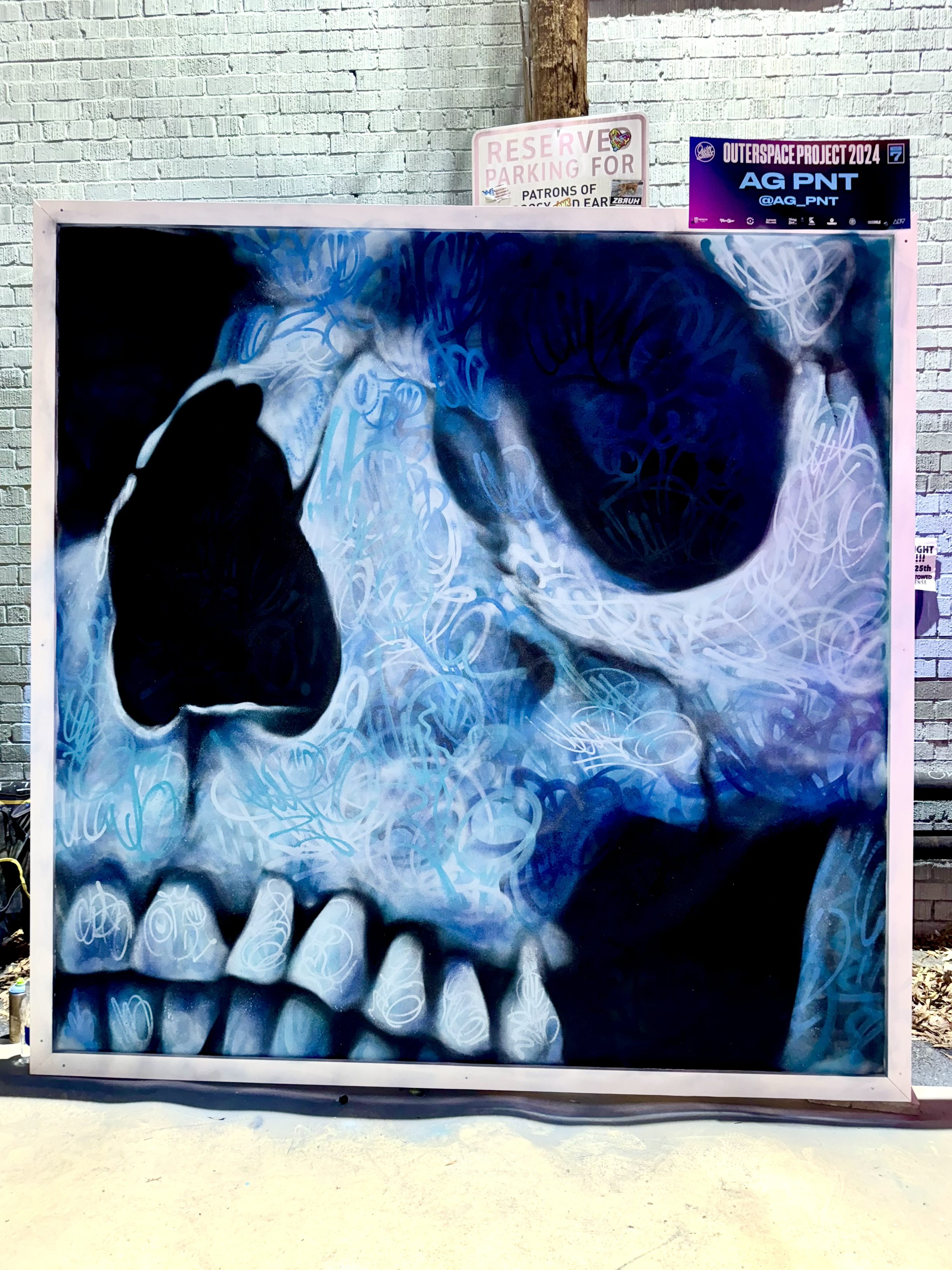 Street art mural of a human face in black, white, and blue shades, with swirling patterns and prominent teeth.