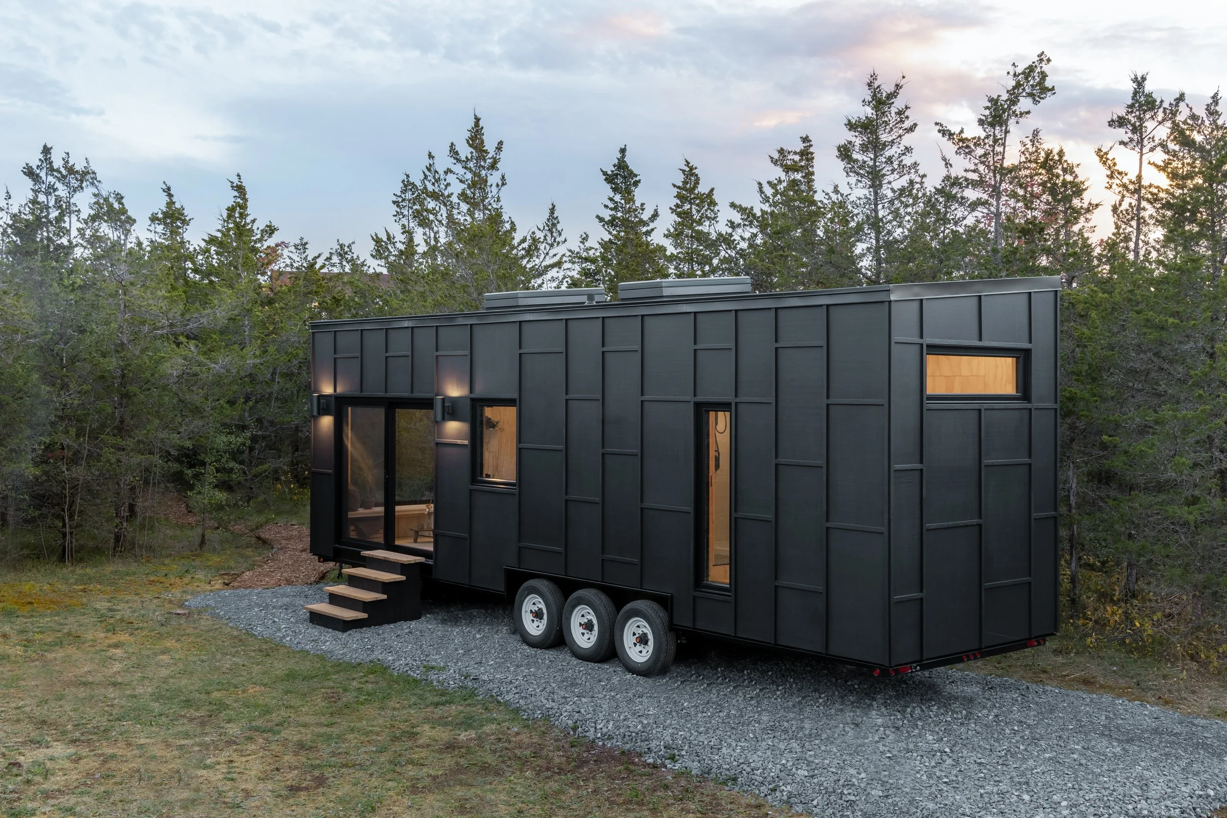 Tiny home on wheels at dusk set over a forested background