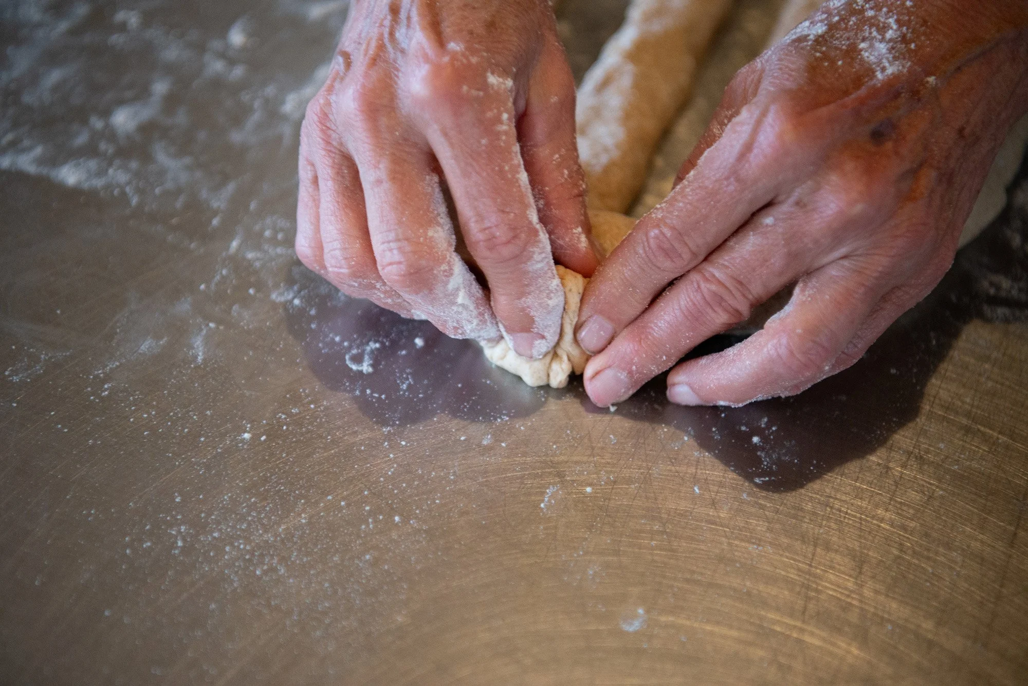 Hands kneading dough on a floured metal surface.