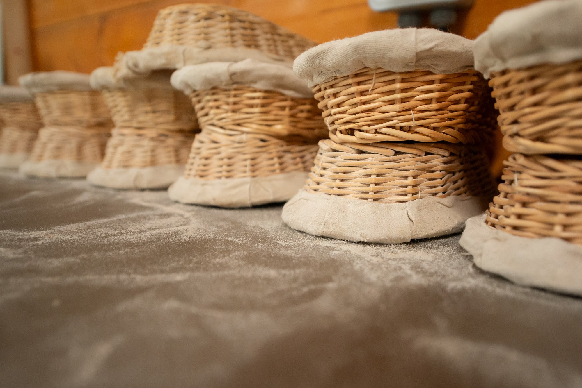 Multiple wicker baskets lined up on a surface, with some dust or flour scattered around.