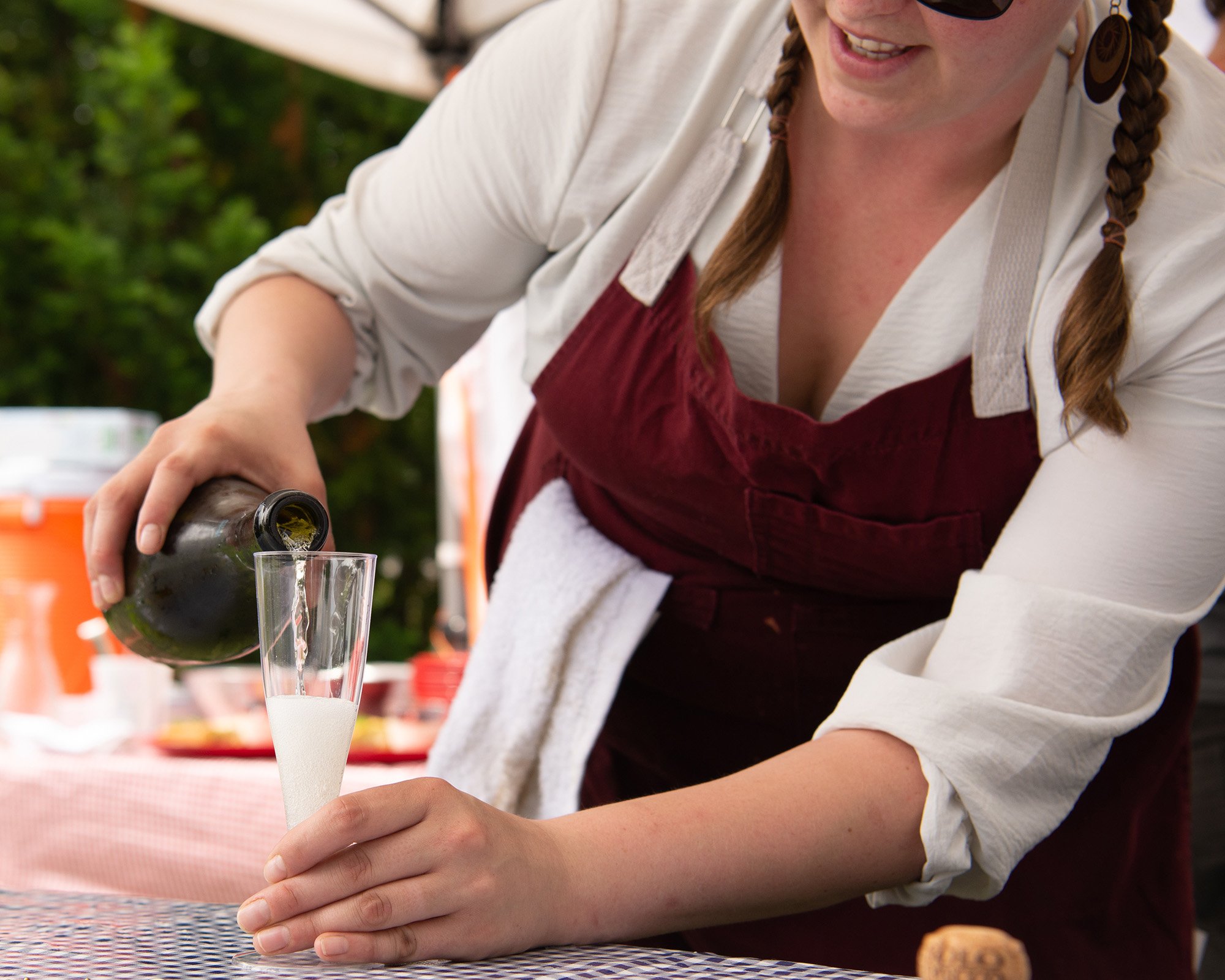 Person pouring sparkling wine into a glass at an outdoor gathering.