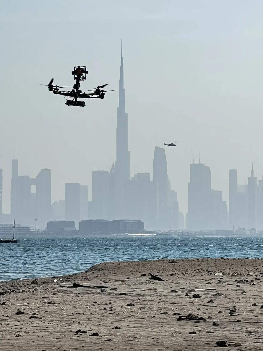 Camera helicopter and drone filming a feature film off the World Islands with the Dubai skyline in haze