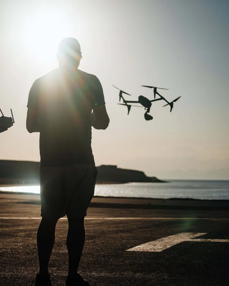 Pilot silhouetted against the sun with an Inspire drone flying beside him