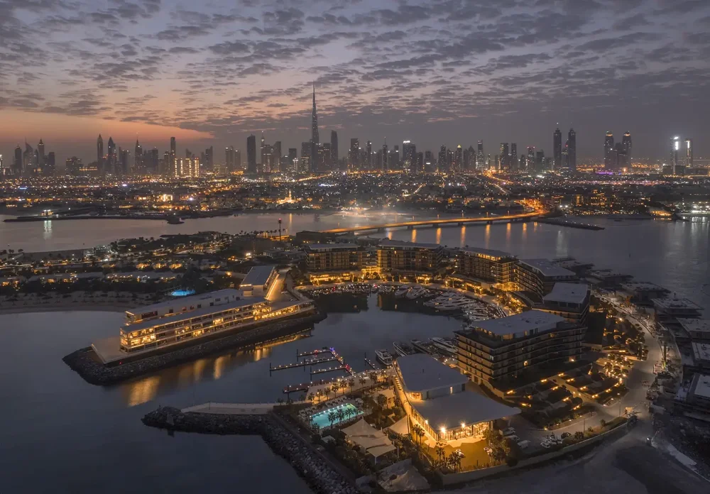 Evening aerial view of an island resort and marina with the Dubai skyline lit up behind