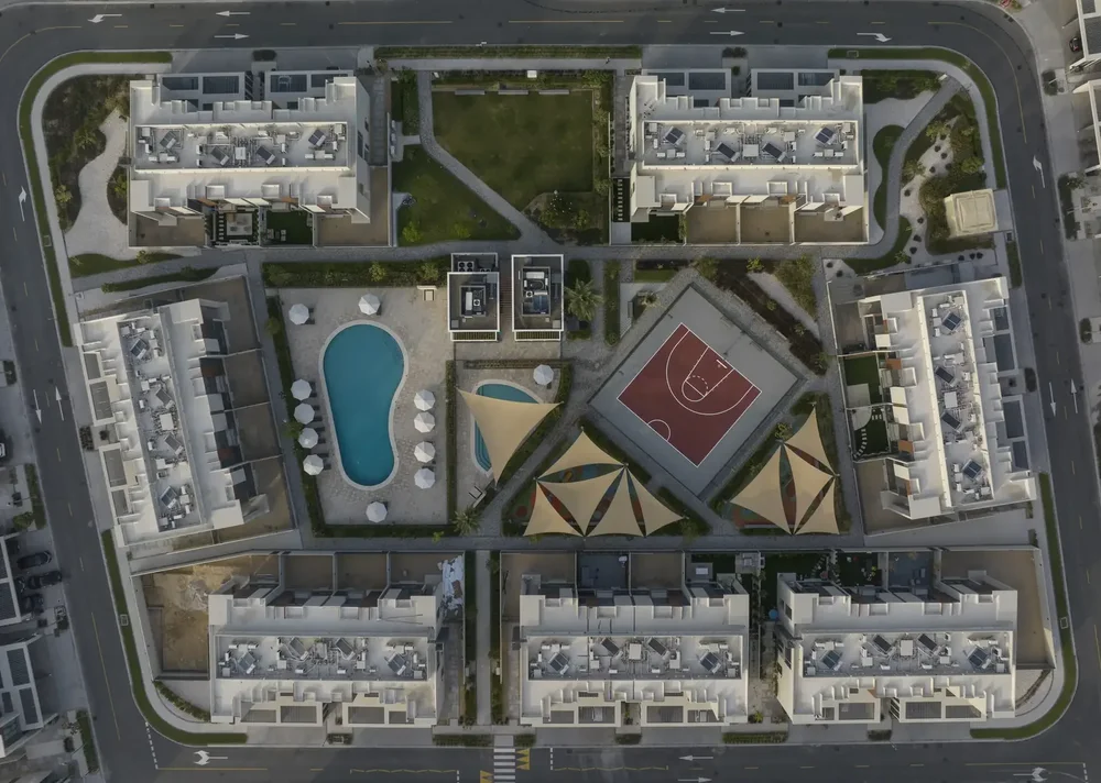 Top-down aerial photo of a residential complex with geometric rooftops and a swimming pool in Dubai