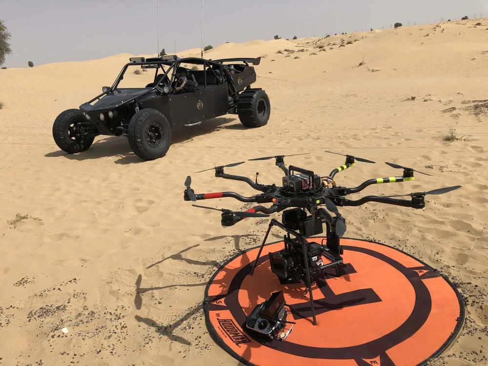 Heavy-lift cinema drone on its landing pad in the Dubai desert, next to a dune buggy used in an action scene for the film Misfits