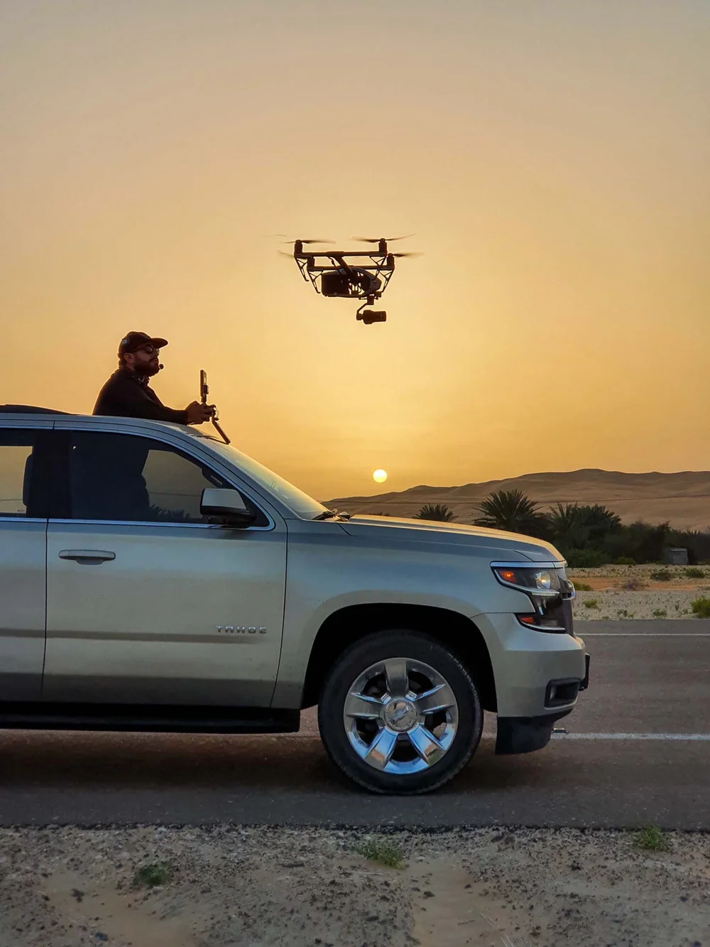 Drone operator filming from a support car during a professional cycling race in the UAE at sunset