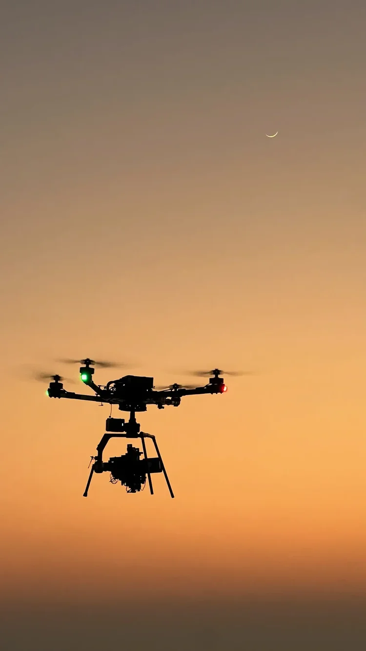Heavy-lift cinema drone hovering against an orange evening sky with the crescent moon