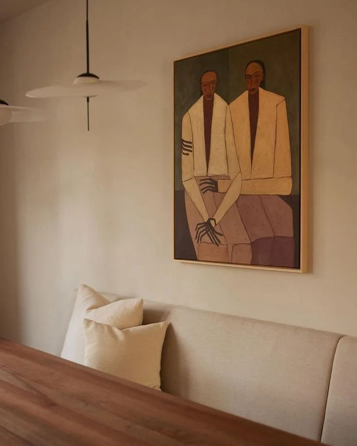 Wall art with two men in jackets, sitting with hands crossed, in a minimalist room.