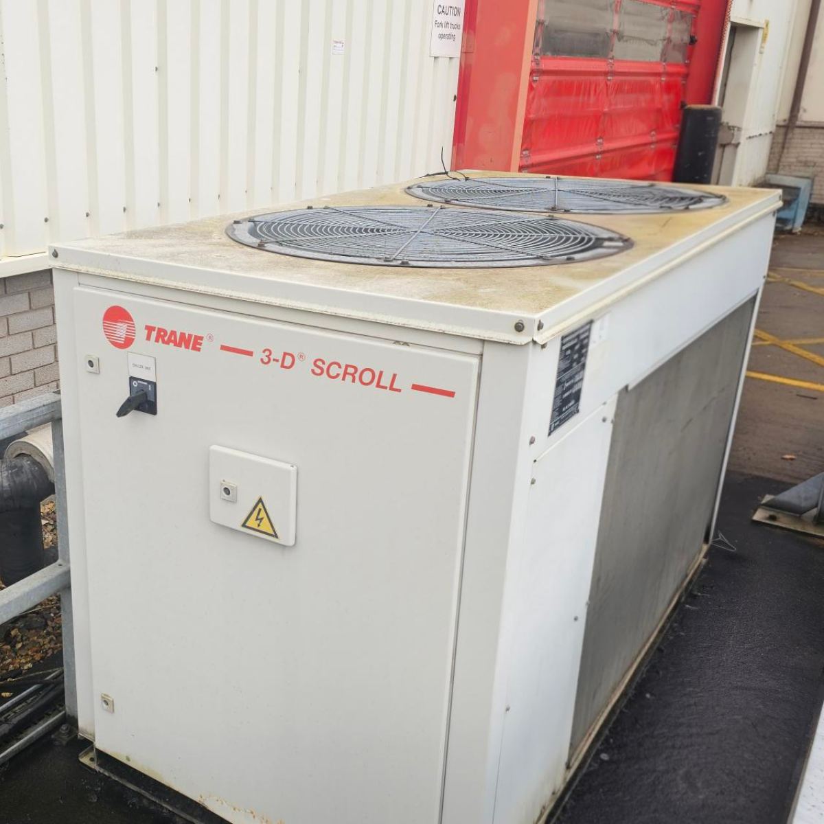 An outdoor air conditioning or refrigeration unit with the brand name Trane, labeled 3-D Scroll, featuring two large fan coils on top.