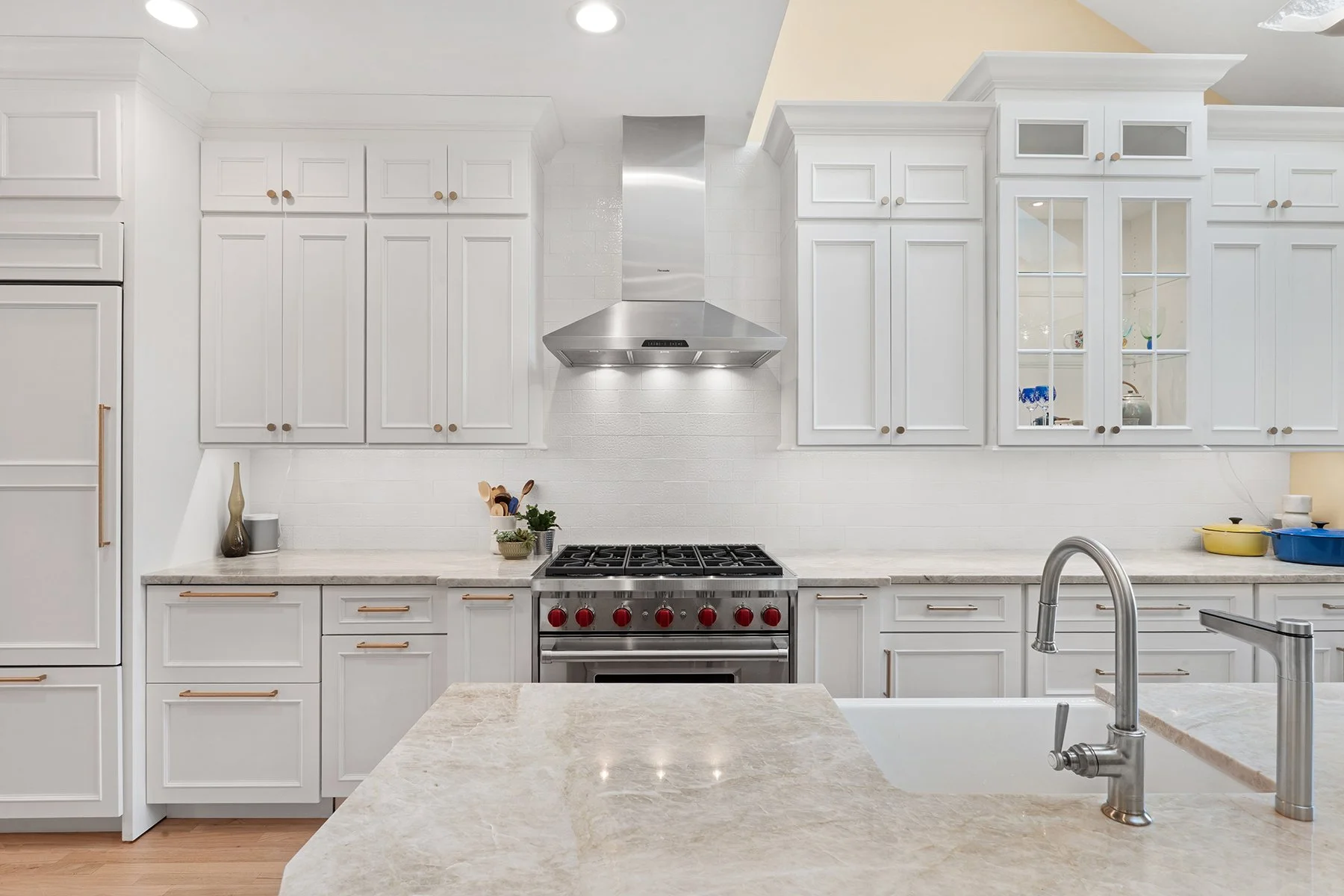 Sleek white cabinetry contrasts with the custom chrome hood and range