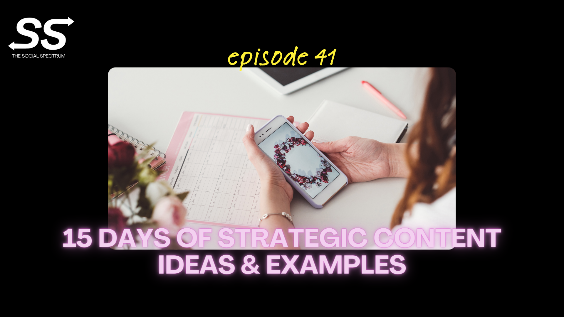 A person holding their cell phone with a monthly planner sitting on their desk