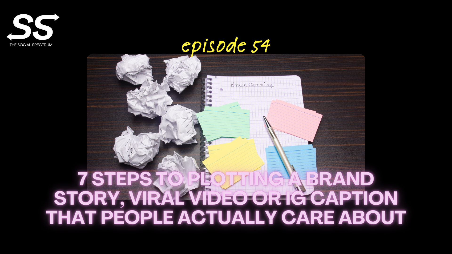 An overhead view of a journal with the word brainstorming written at the top, with bunched up paper balls next to it and colorful notecards sitting atop it