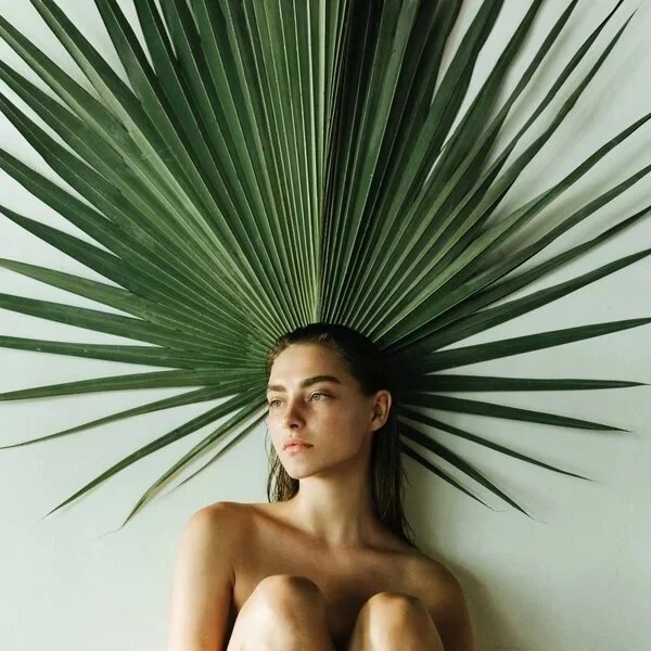 Young woman sitting with a large palm leaf behind her head, creating a fan shape.