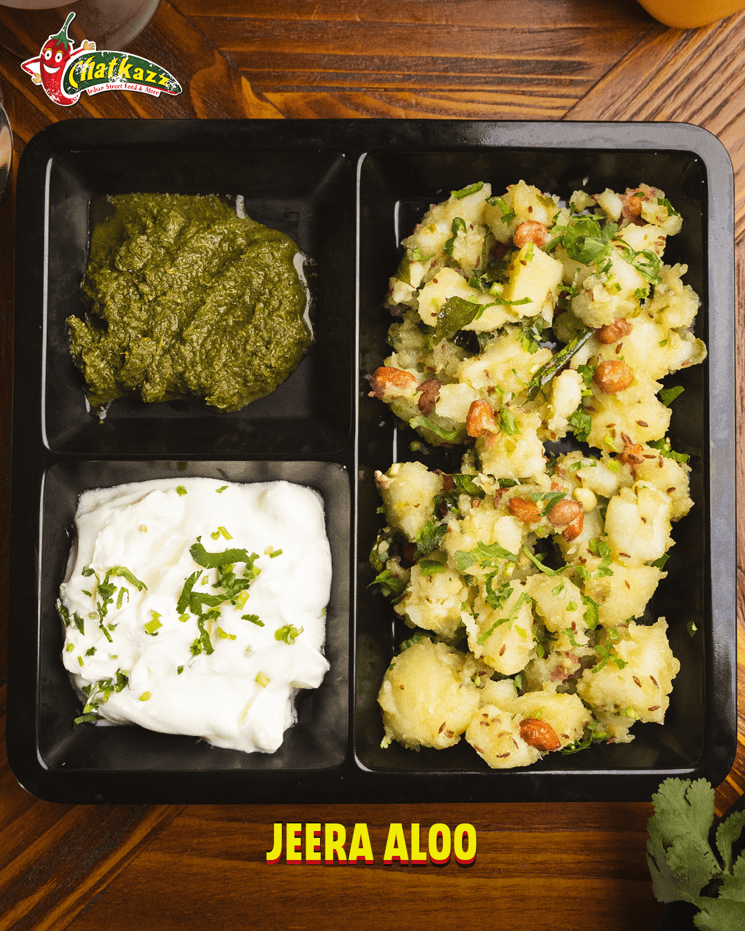 Jeera Aloo served in a black tray with green chutney and yogurt dip at Chatkazz.