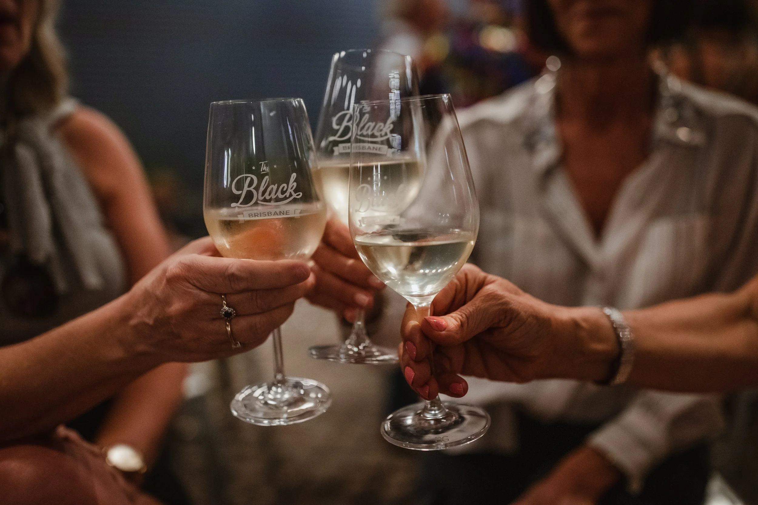 Four people clinking wine glasses with white wine at a gathering or celebration.