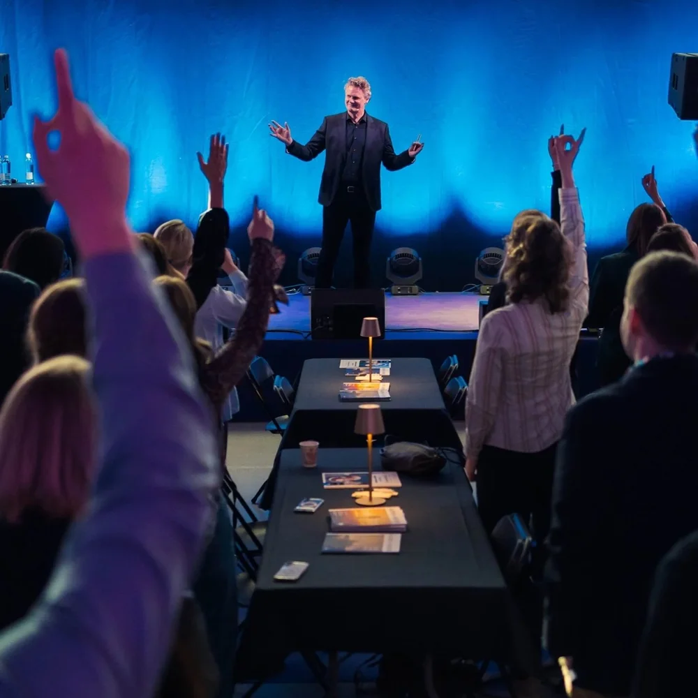 Caspar Craven giving a keynote to a leadership audience, hands raised across the room