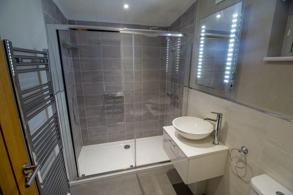 Modern twin bedroom en-suite bathroom at Teal Lodge Cornwall, with a spacious double shower, basin, illuminated mirror and heated towel rail.