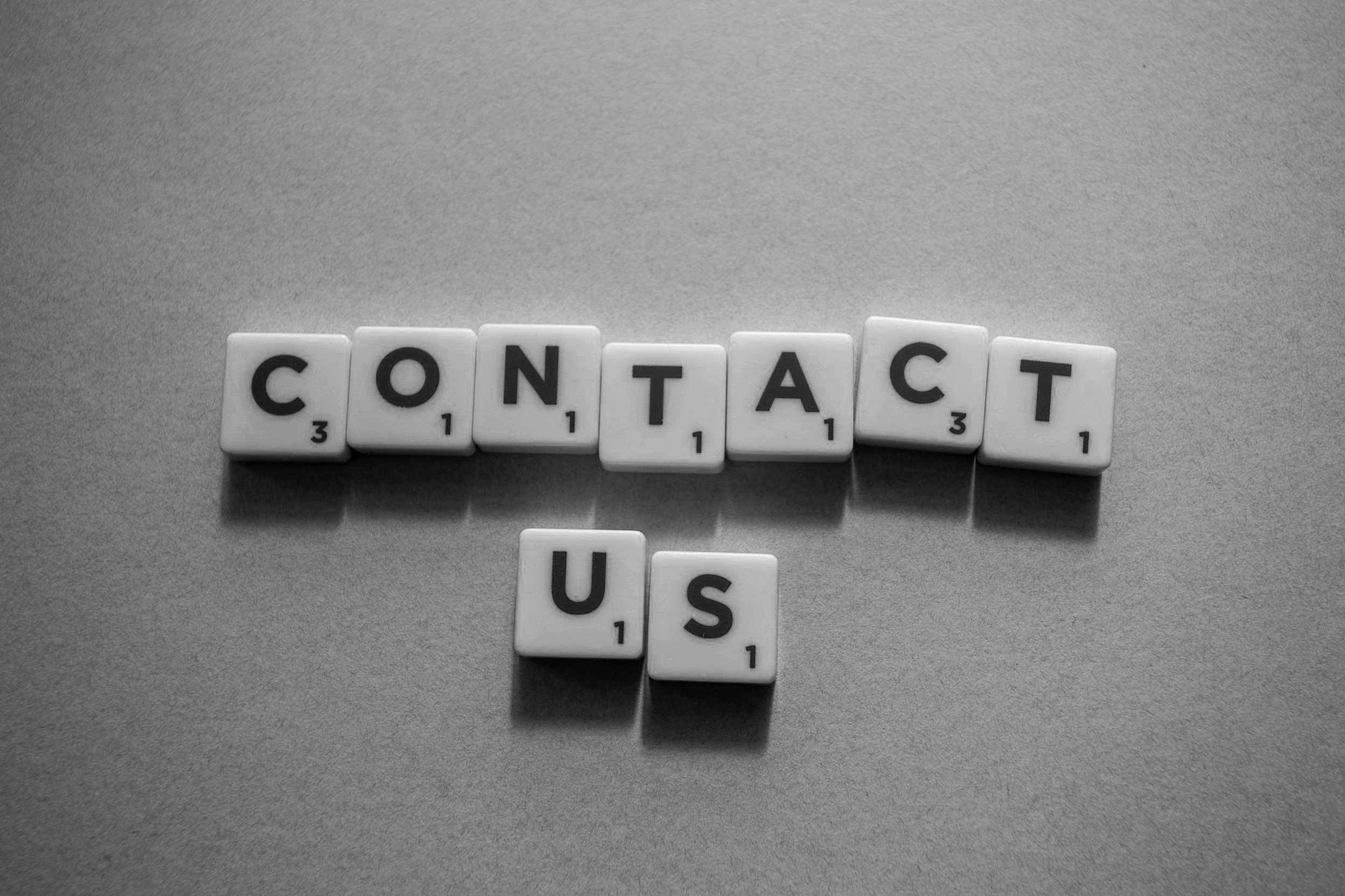 Scrabble tiles spelling "CONTACT US" on a gray surface.