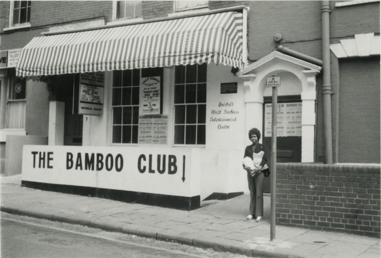 Black and white photograph of a woman stood outside the entrance to The Bamboo Club