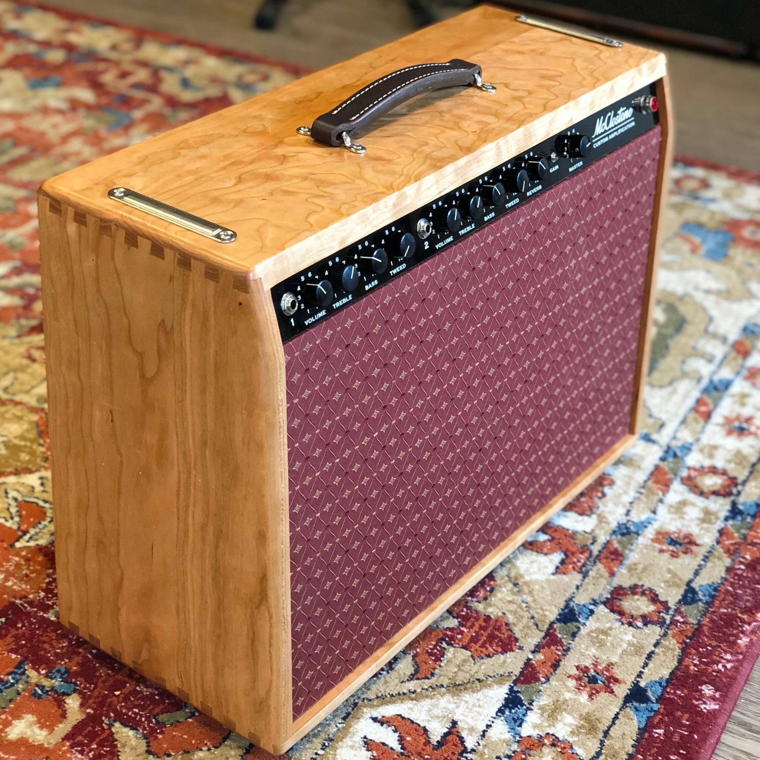 A cherry wood custom deluxe reverb with a red fabric grille, control knobs, and a handle on top, and awesome tone and versatility.