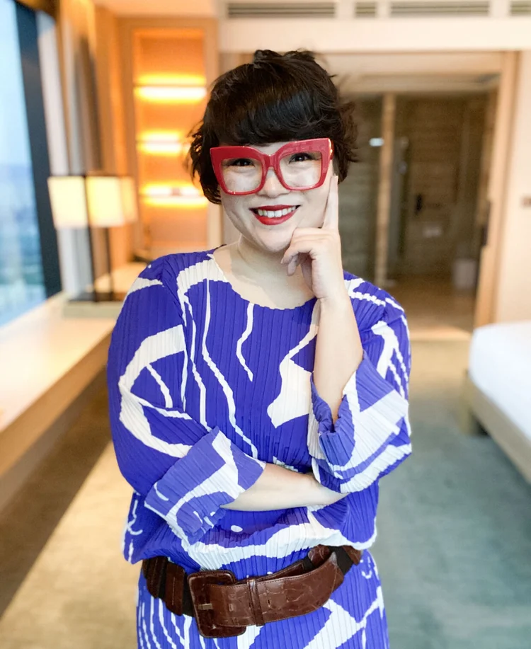 Simone wearing a blue & white dress & chunky brown leather belt. She's wearing bright red lipstick & massive chunky red glasses.