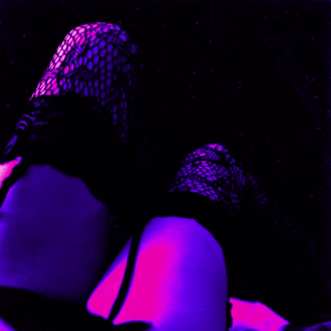 Person sitting in purple and blue lighting, wearing fishnet stockings and shorts, with the view of their legs and feet.