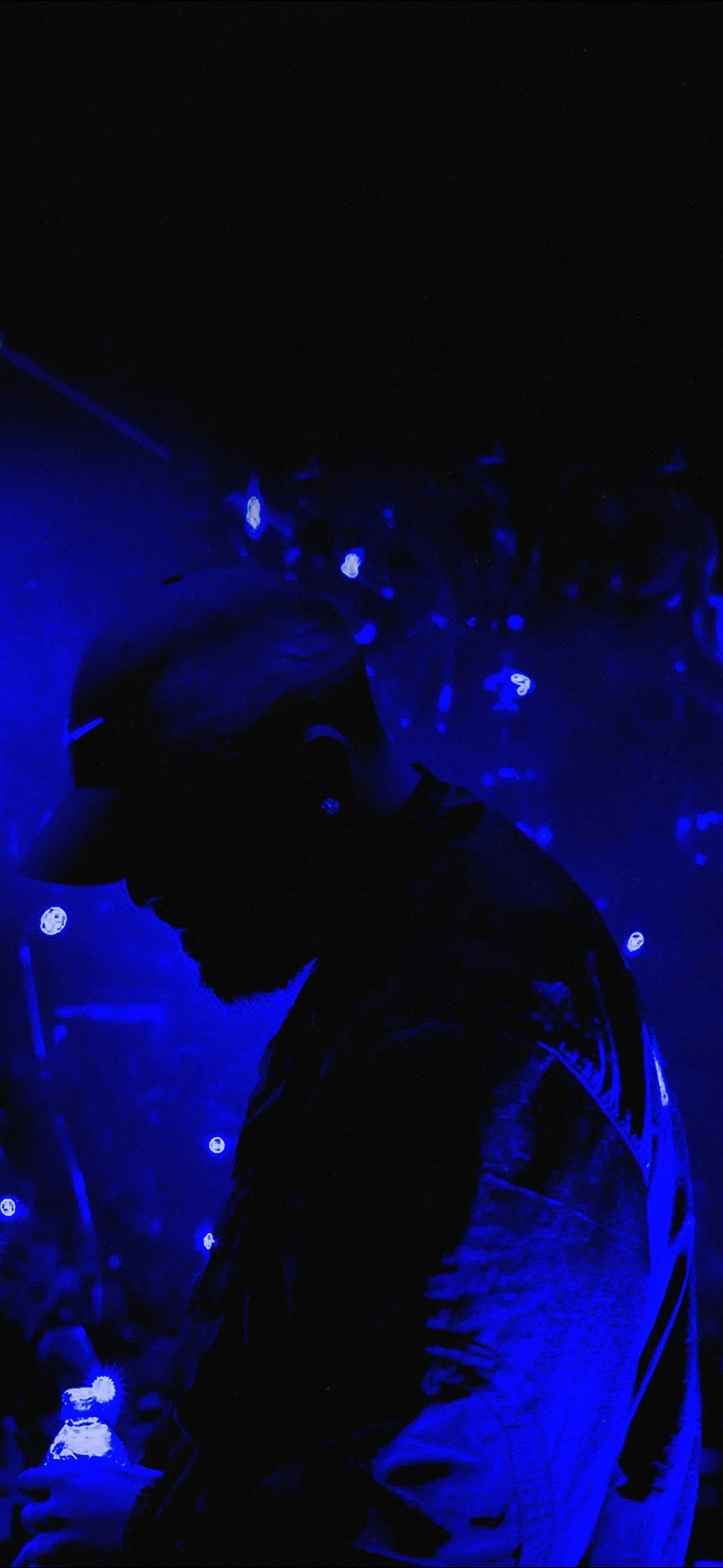 Drake Phone Wallpaper. A silhouette of a man wearing a helmet and jacket, holding a drink, illuminated by blue lighting at a dark, possibly nightclub or concert, setting.
