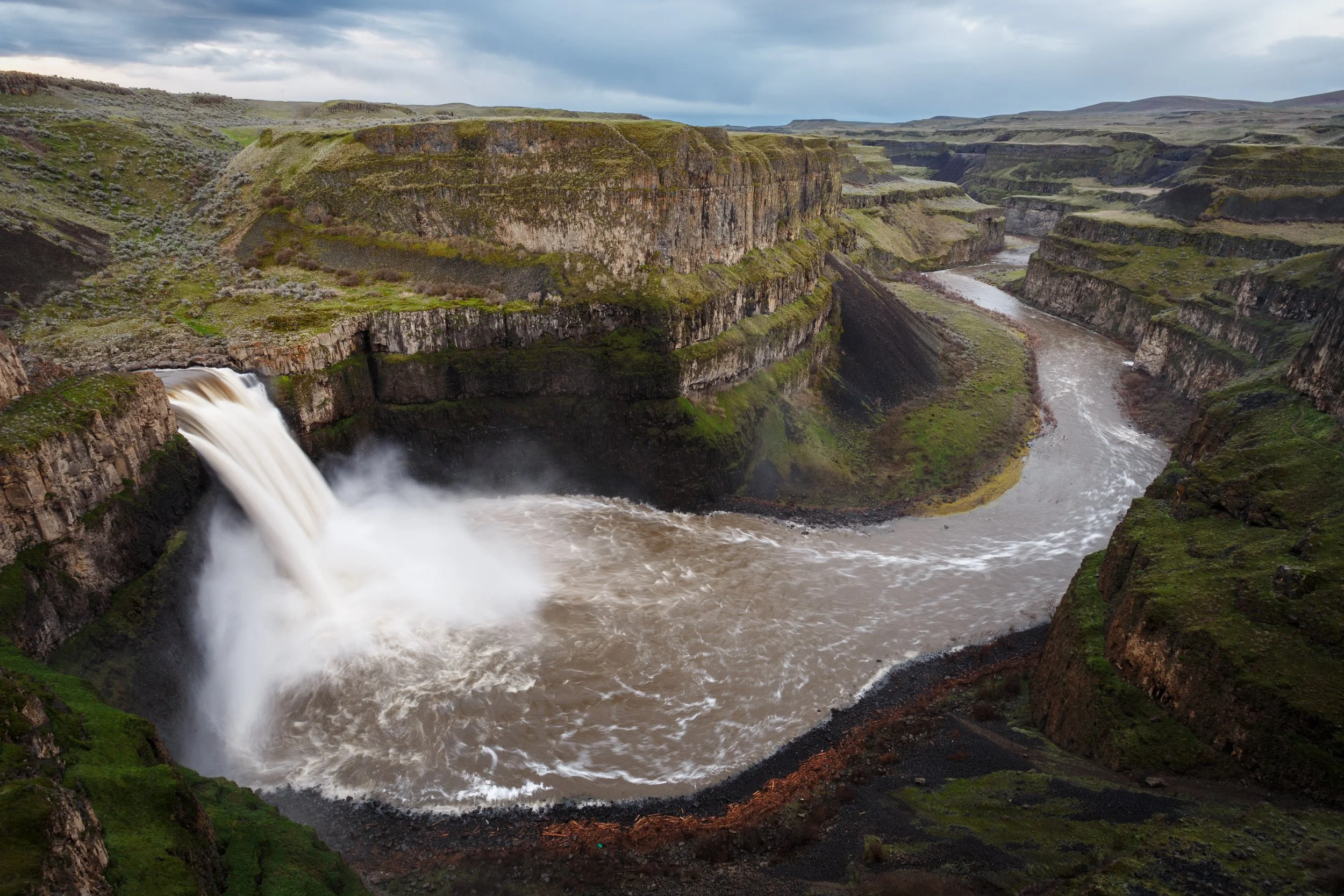 A large canyon with a waterfall flowing into a river that winds through the canyon.