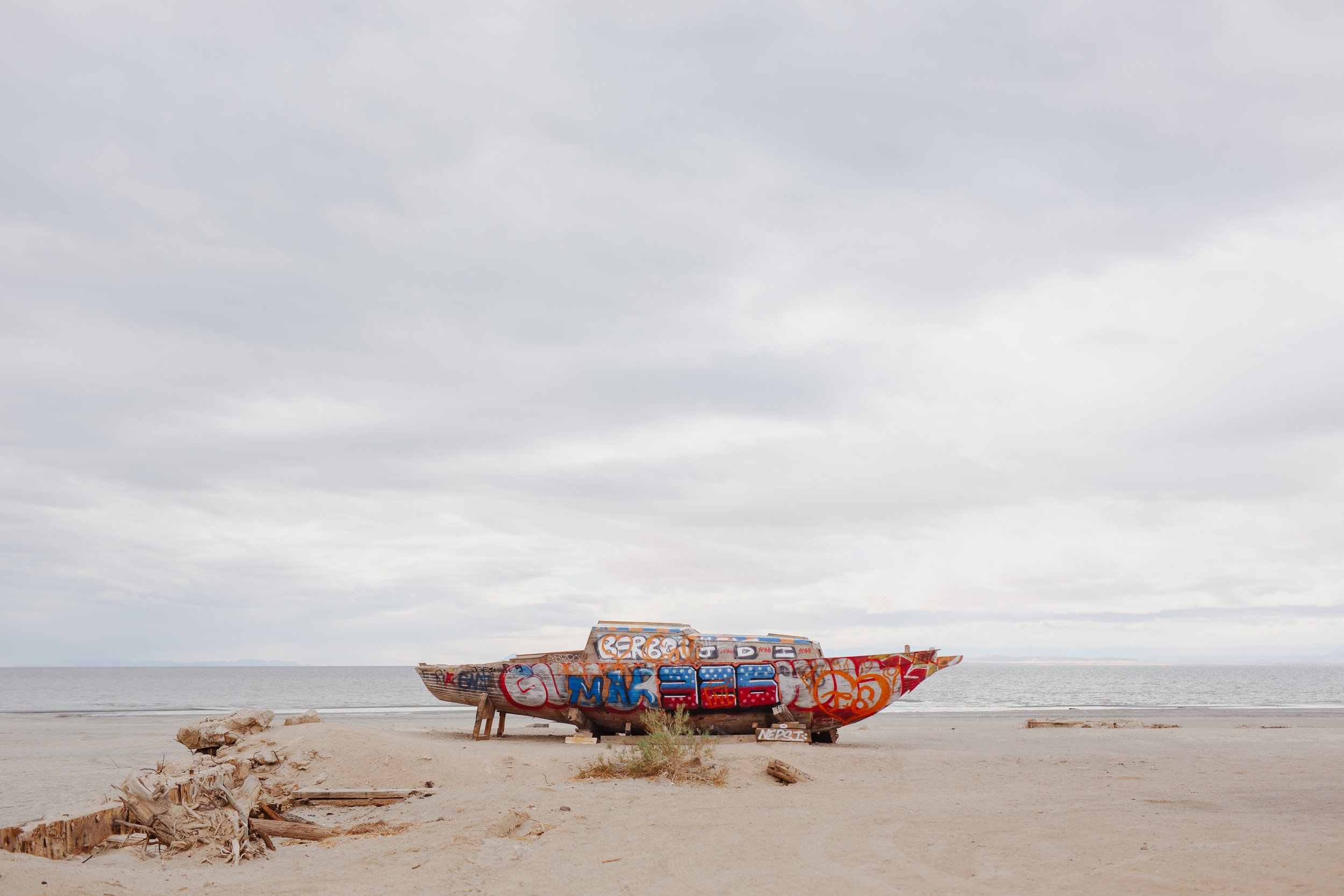 Graffiti-covered boat on a sandy beach under a cloudy sky.