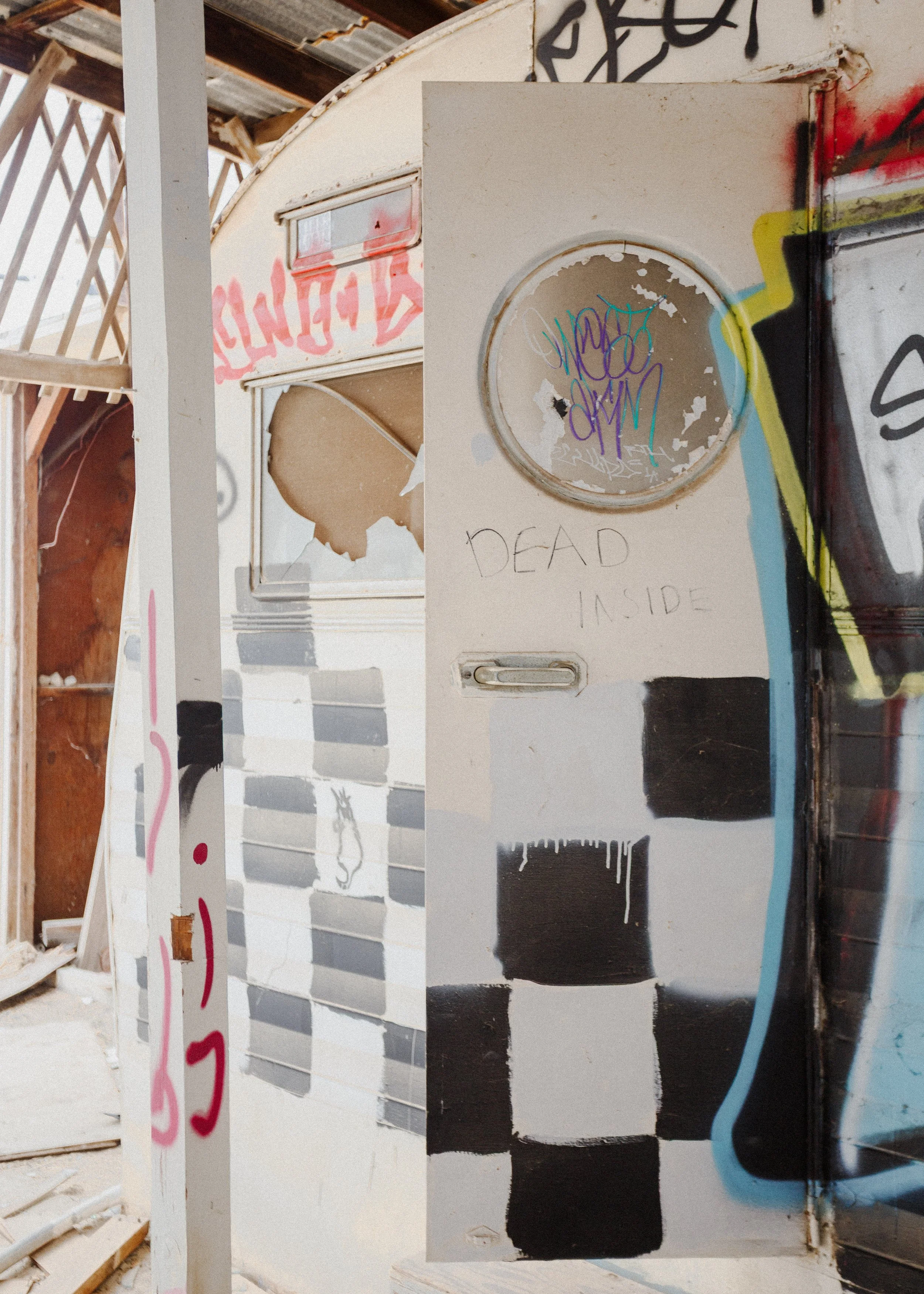 An abandoned, graffitied trailer or camper in a dilapidated building with graffiti and torn posters.