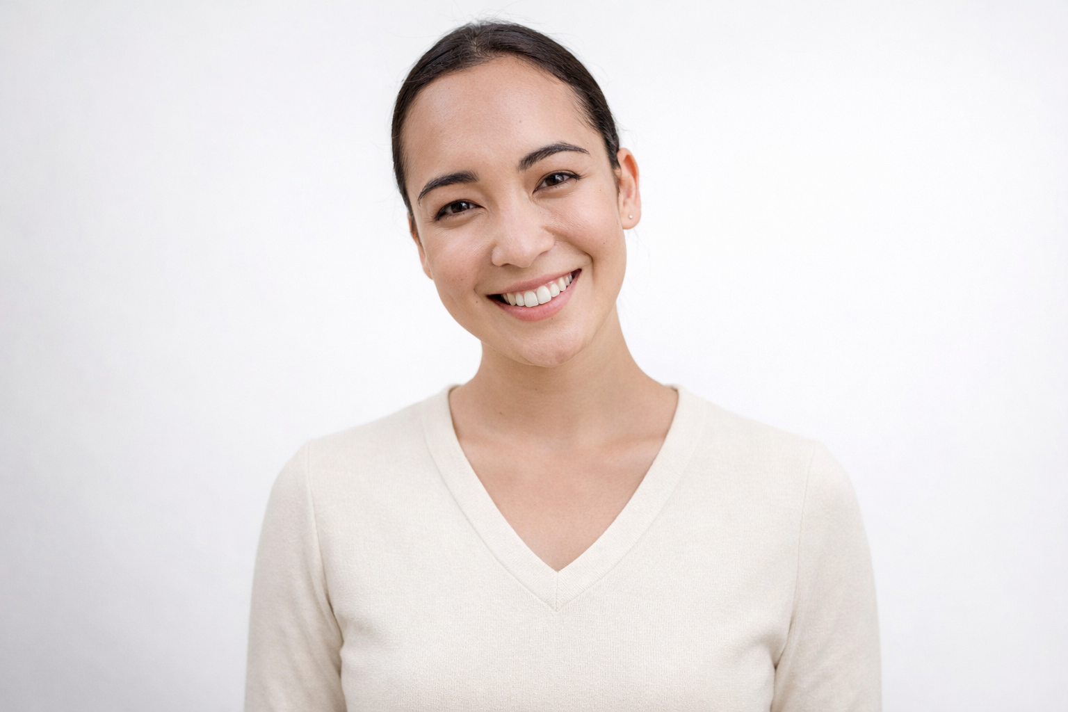 Smiling woman with dark hair in a beige V-neck top standing against a white background.
