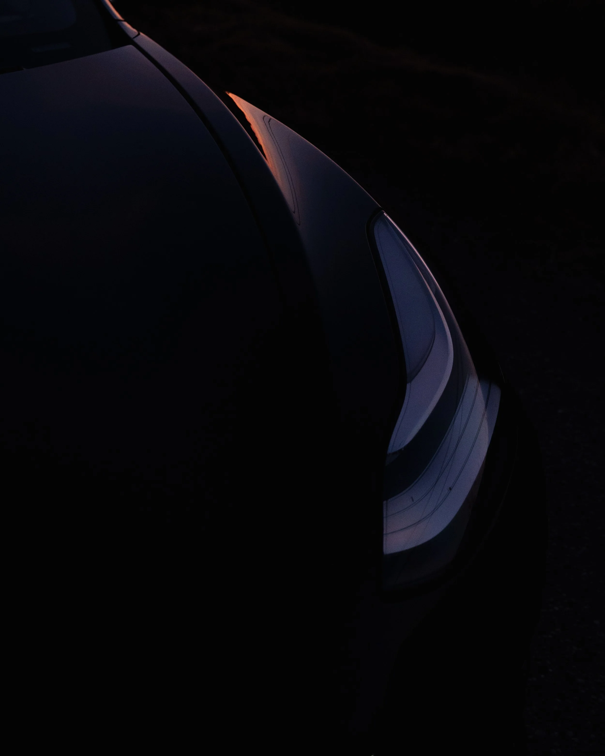 Close-up of a car's front end, showing headlights and hood, in a dark setting with minimal lighting.
