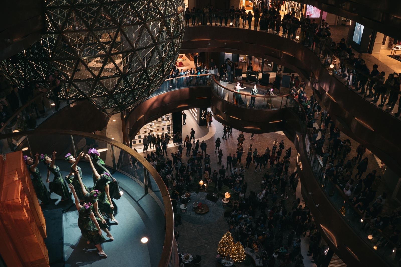Performers in green and red costumes dance in front of the ornate "Gold Ball" atrium architecture and a glowing Christmas tree at K11 MUSEA.