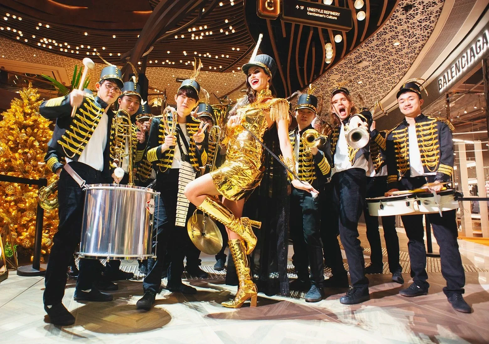 A festive marching band with drummers and a lead performer in a shimmering gold outfit posing during the K11 MUSEA opening ceremony in Hong Kong.