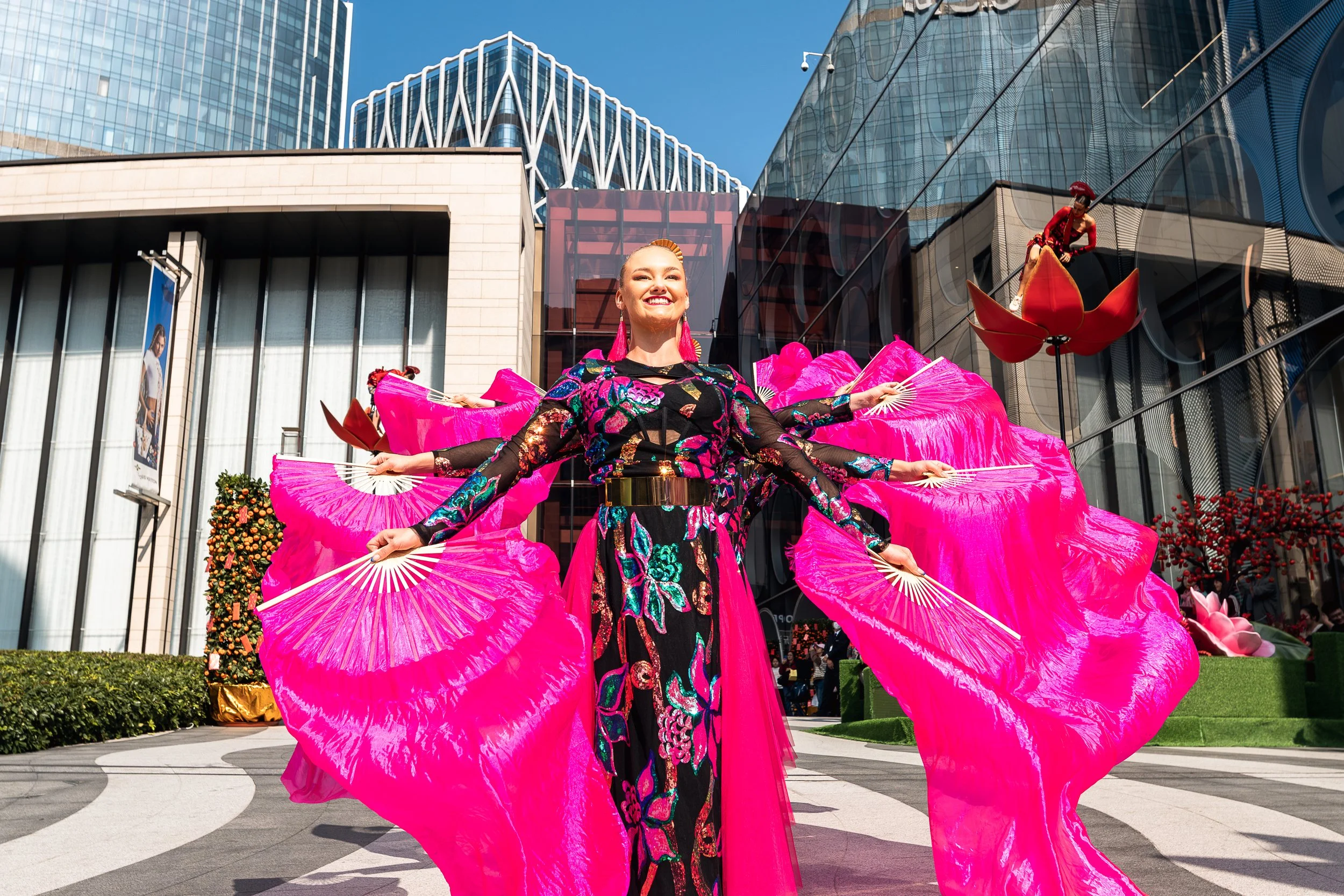 A synchronized group dance routine by BPM Productions Hong Kong performers with large pink fans in front of the City of Dreams casino entrance