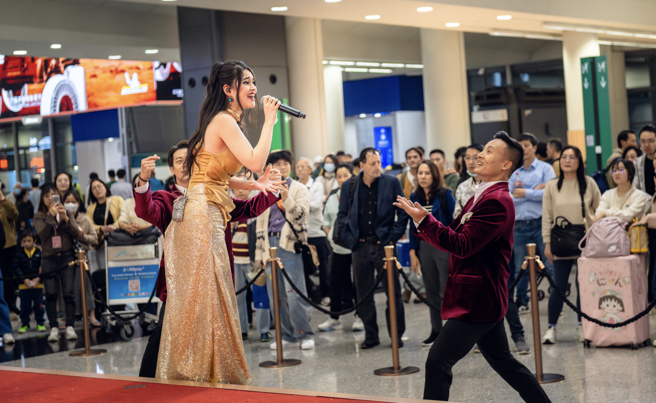 A female vocalist and performers from BPM Productions Hong Kong engaging a large crowd of travelers during a live Christmas concert at the HKIA Arrivals Hall.