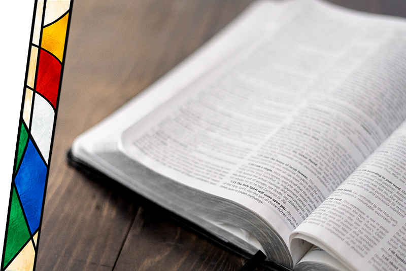 An open Bible on a wooden table with a stained glass lamp nearby.
