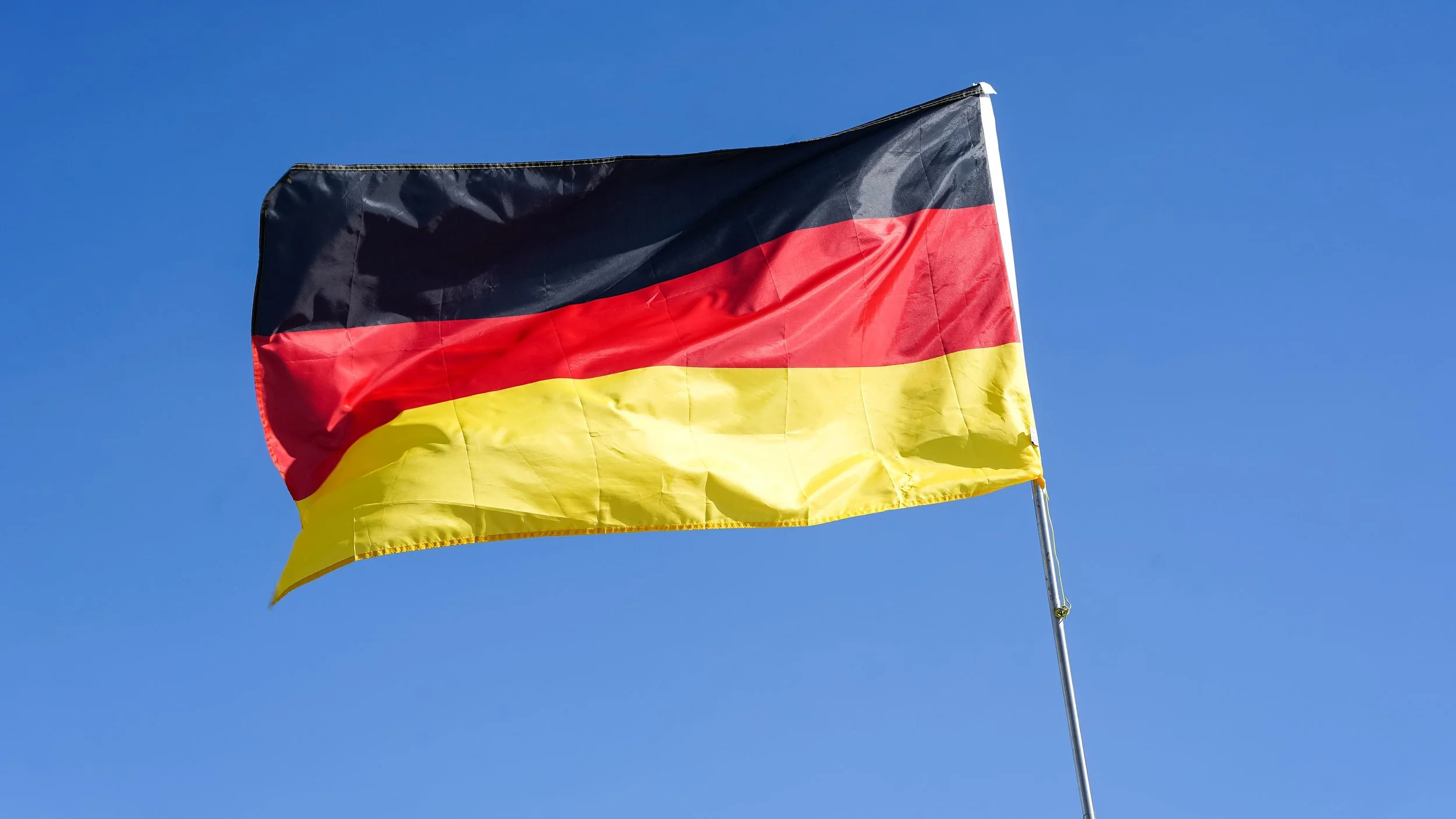 German national flag flying in the wind against a clear blue sky.