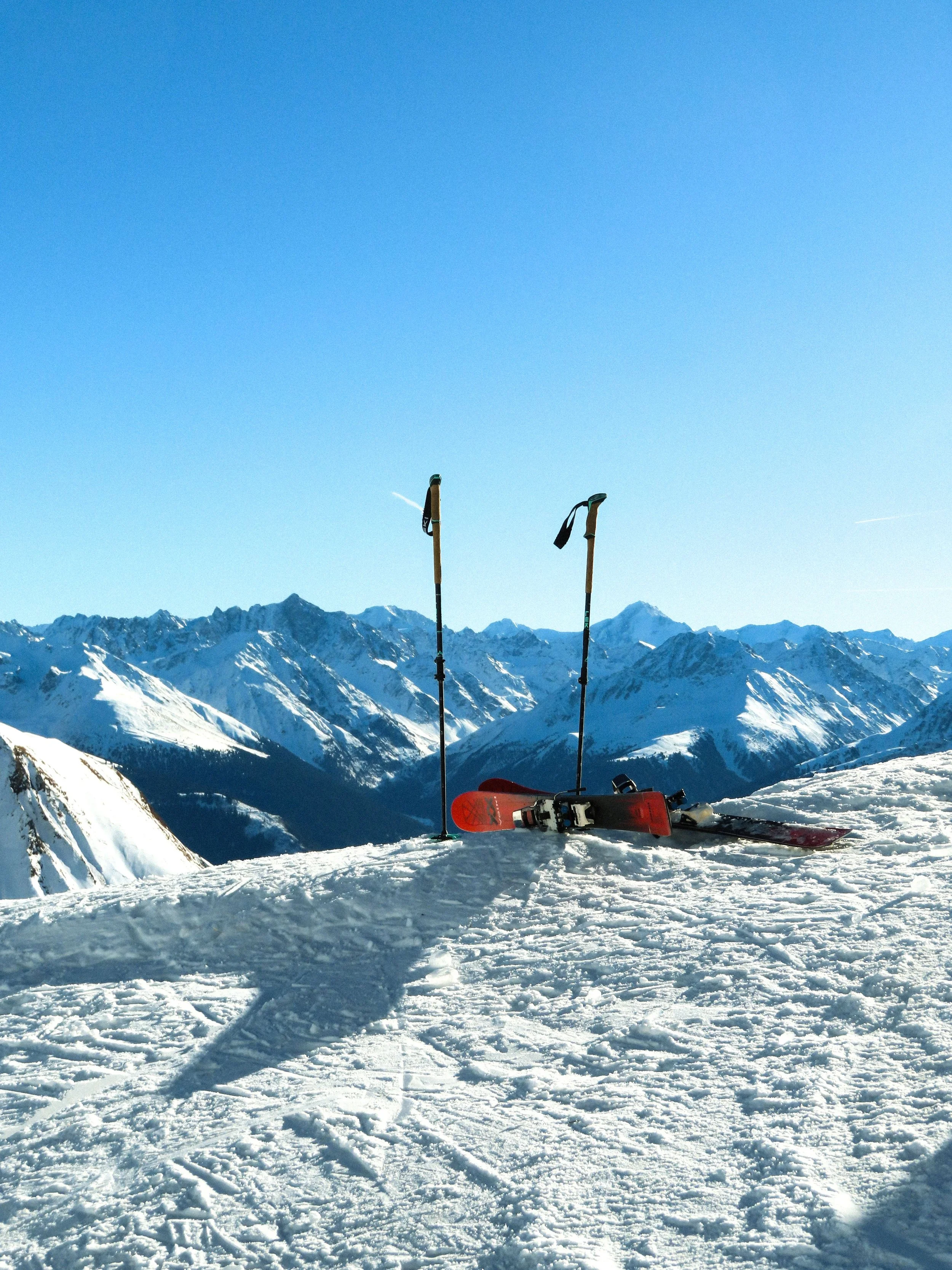 Snow-covered mountain landscape with two ski poles and a snowboard resting on the snow.