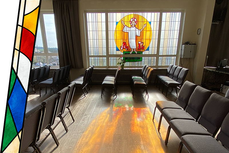 Empty church or chapel waiting room with chairs facing a stained glass window of Jesus Christ with open arms.
