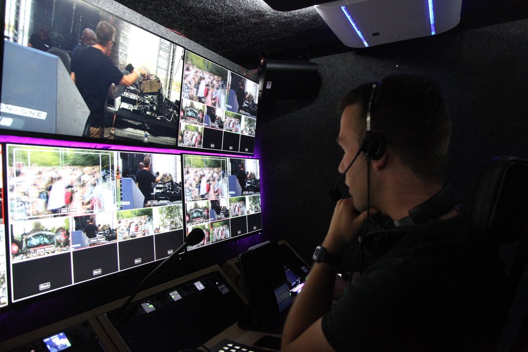 Een persoon in een controlekamer met meerdere schermen die verschillende camerahoeken van een evenement tonen.